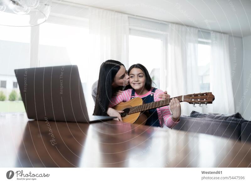 Mother kissing daugher playing guitar in front of laptop mother mommy mothers ma mummy mama daughter daughters Laptop Computers laptops notebook smiling smile