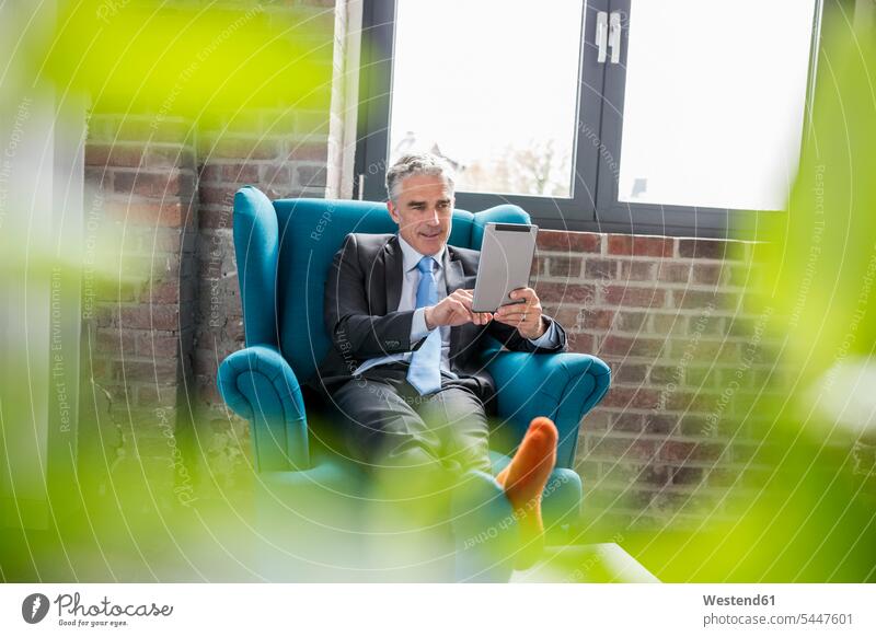 Mature businessman sitting in arm chair, using digital tablet Businessman Business man Businessmen Business men Seated working At Work digitizer Tablet Computer