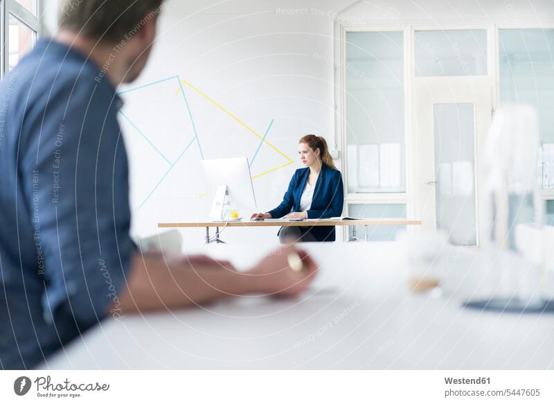 Businesswoman working in office with colleague sitting in foreground offices office room office rooms At Work Seated colleagues businesswoman businesswomen