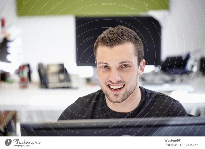 Young man working in office, looking at camera sitting Seated young entrepreneur young entrepreneurs start-up entrepreneur At Work portrait portraits smiling