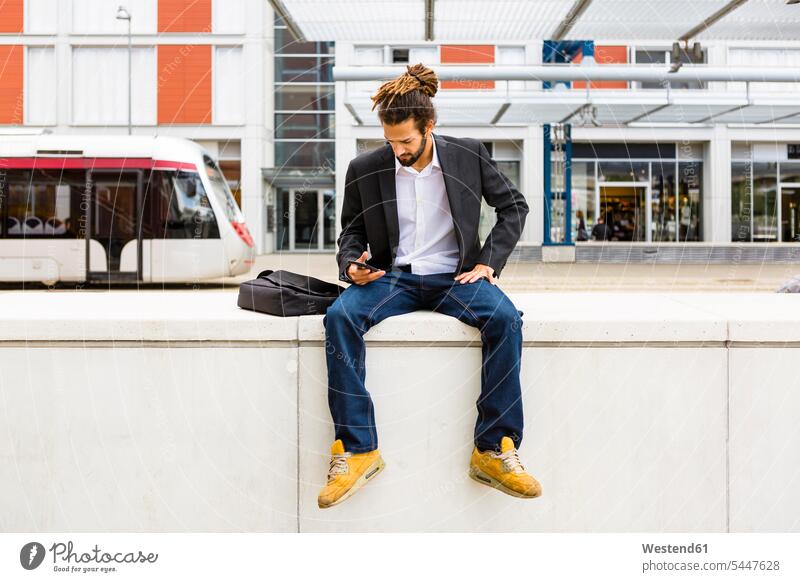 Young businessman with dreadlocks using smartphone while waiting at station Businessman Business man Businessmen Business men Smartphone iPhone Smartphones