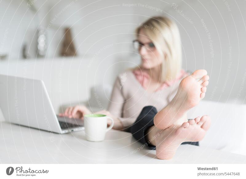 Woman sitting at table with feet up using laptop woman females women Laptop Computers laptops notebook Table Tables Adults grown-ups grownups adult people