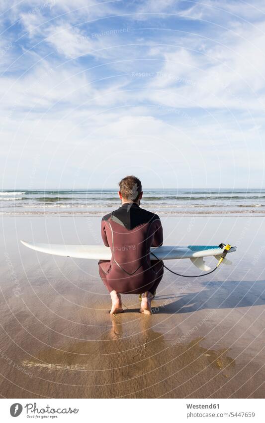 Man with surfboard crouching on the beach beaches surfer surfers man men males surfboards surfing surf ride surf riding Surfboarding water sports Water Sport