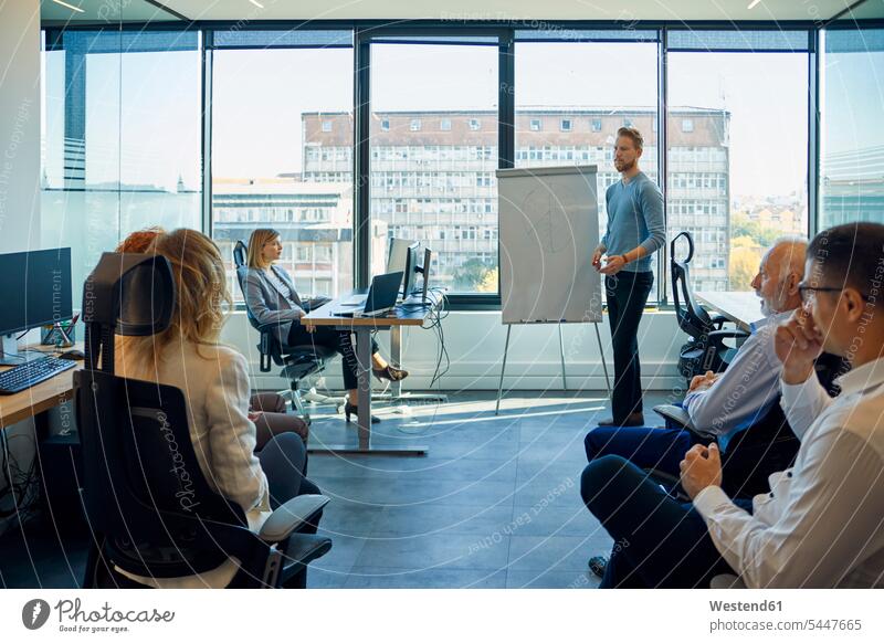 Man leading a presentation at flip chart in office team Business Meeting business conference meeting presentations group of people Group groups of people