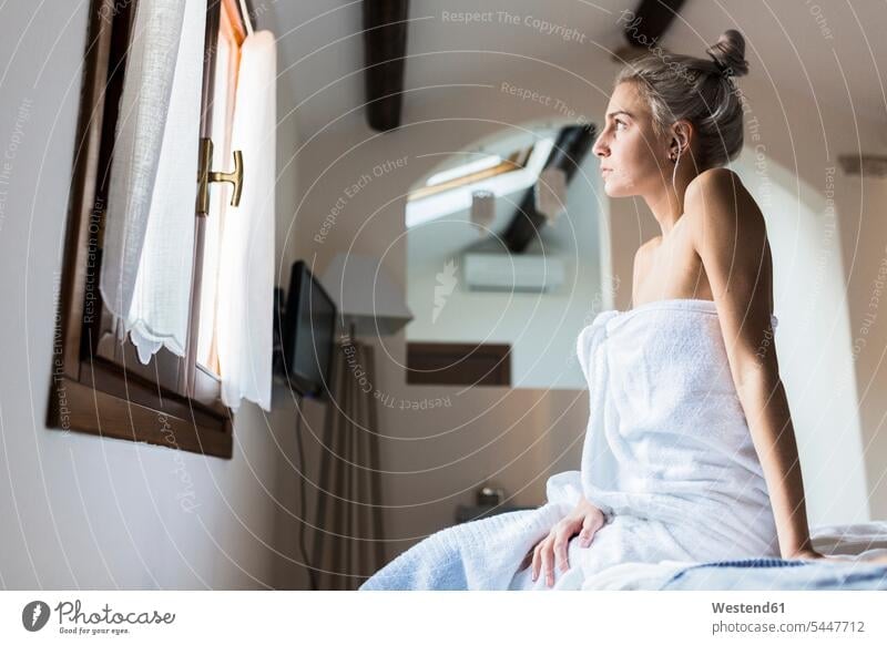 Young woman wrapped in a towel sitting on bed looking out of window windows females women view seeing viewing Seated towels beds Adults grown-ups grownups adult