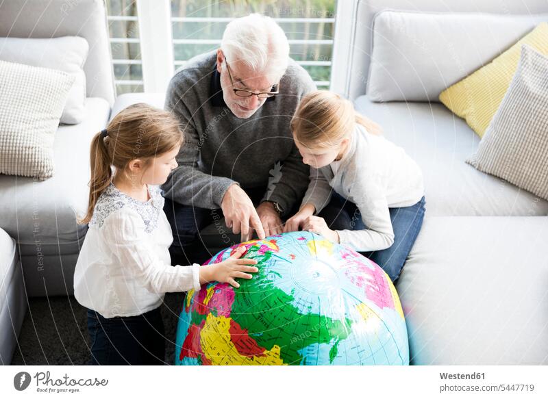 Two girls and grandfather with globe in living room living rooms livingroom females grandpas granddads grandfathers globes domestic room domestic rooms child