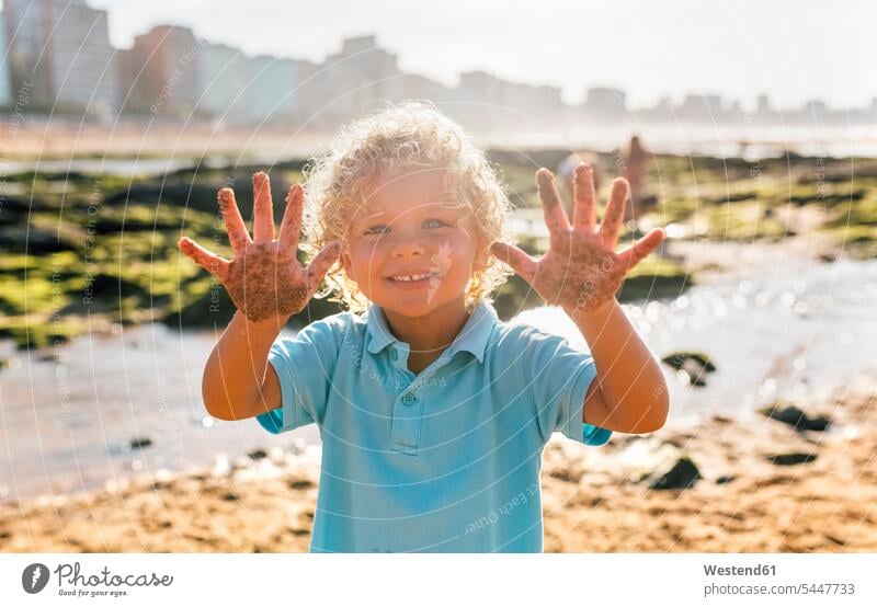 Portrait of smiling little boy showing his sandy hands on the beach portrait portraits boys males human hand human hands child children kid kids people persons