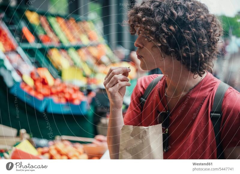 Young man eating cherries in front of street fruit stand men males fruit stall Adults grown-ups grownups adult people persons human being humans human beings