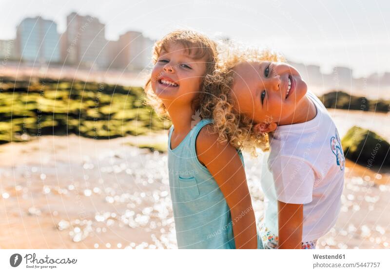 Portrait of happy little boy and girl standing bback to back on the beach portrait portraits boys males females girls beaches child children kid kids people