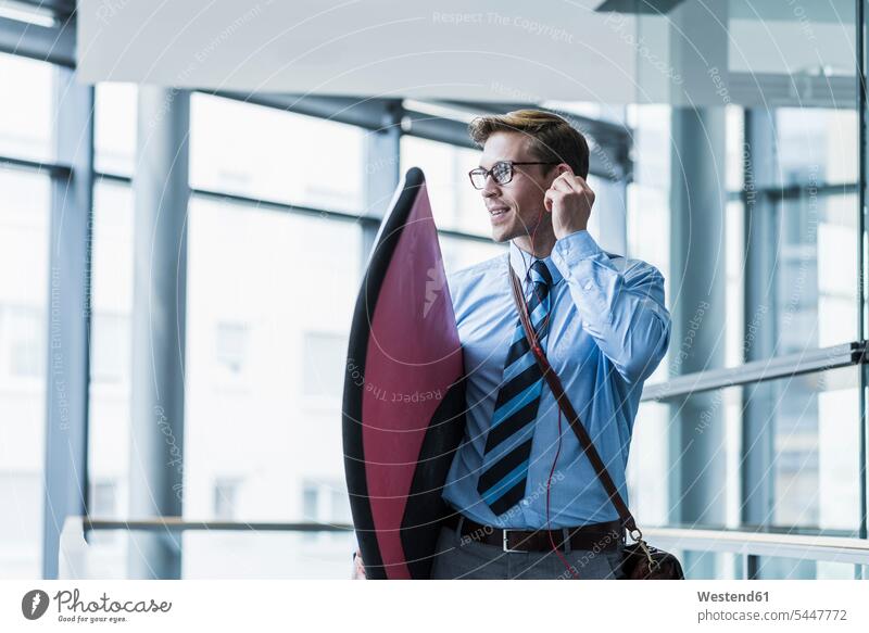 Businessman with earphones carrying surfboard in office Business man Businessmen Business men surfboards business people businesspeople business world
