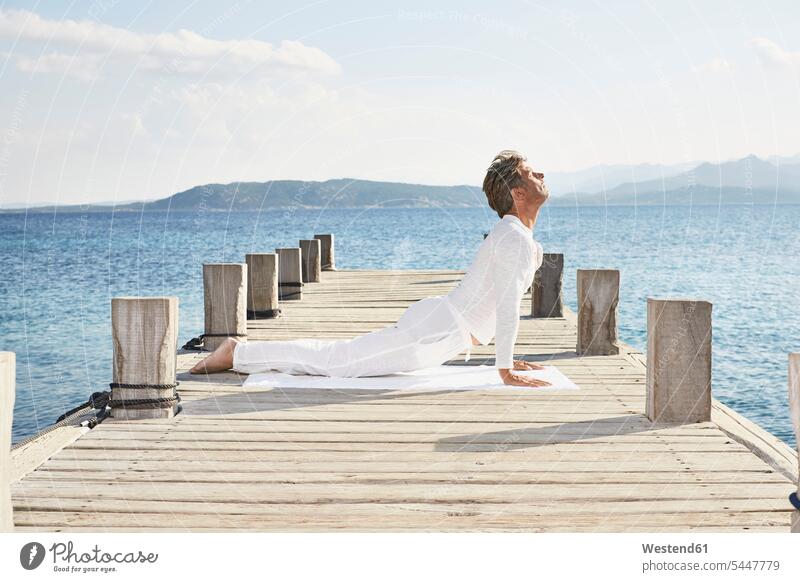 Mature man doing yoga exercise on jetty men males mindfulness aware awareness self-care relaxation exercise relaxed relaxing Adults grown-ups grownups adult