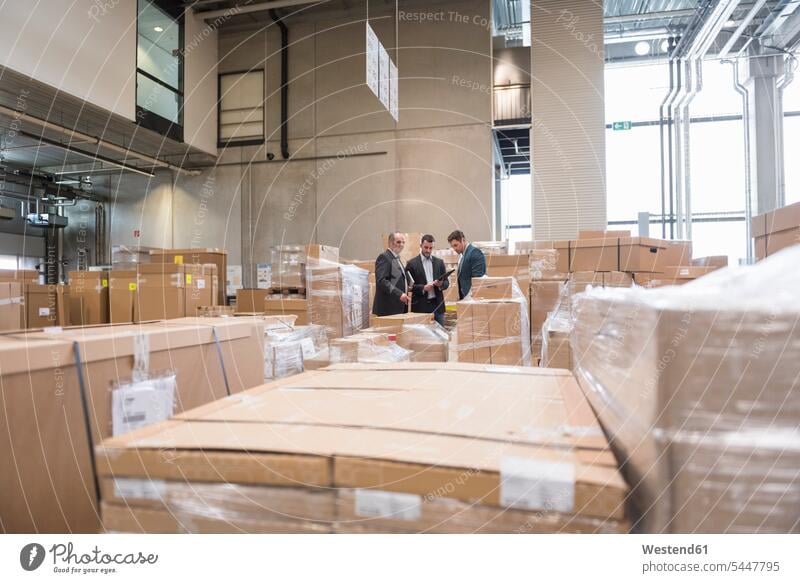Three men in factory warehouse surrounded by cardboard boxes working At Work man males Businessman Business man Businessmen Business men storehouse storage
