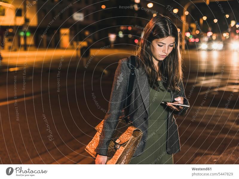 Young businesswoman with leather bag looking at cell phone by night females women at night nite night photography Adults grown-ups grownups adult people persons