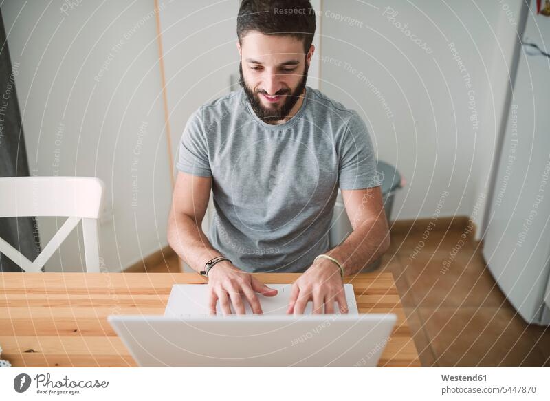 Young man sitting at home, using laptop young men males Surfing the Net Seated typing type Laptop Computers laptops notebook using a laptop Using Laptops