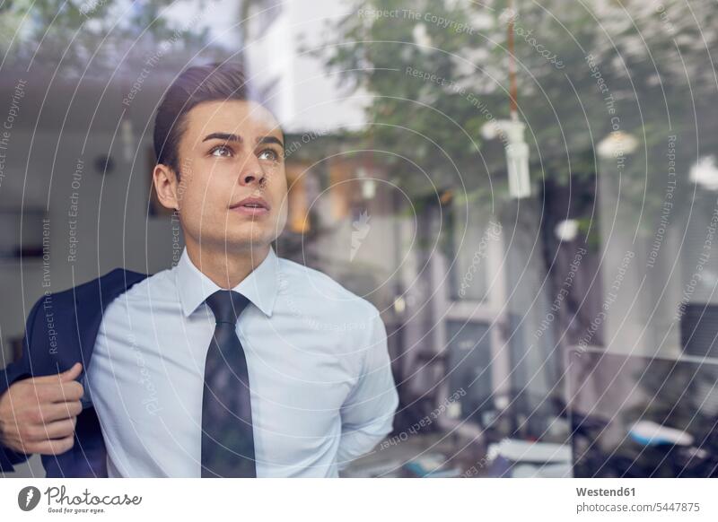 Portrait of young businessman behind glass pane in office putting on his jacket Businessman Business man Businessmen Business men portrait portraits window