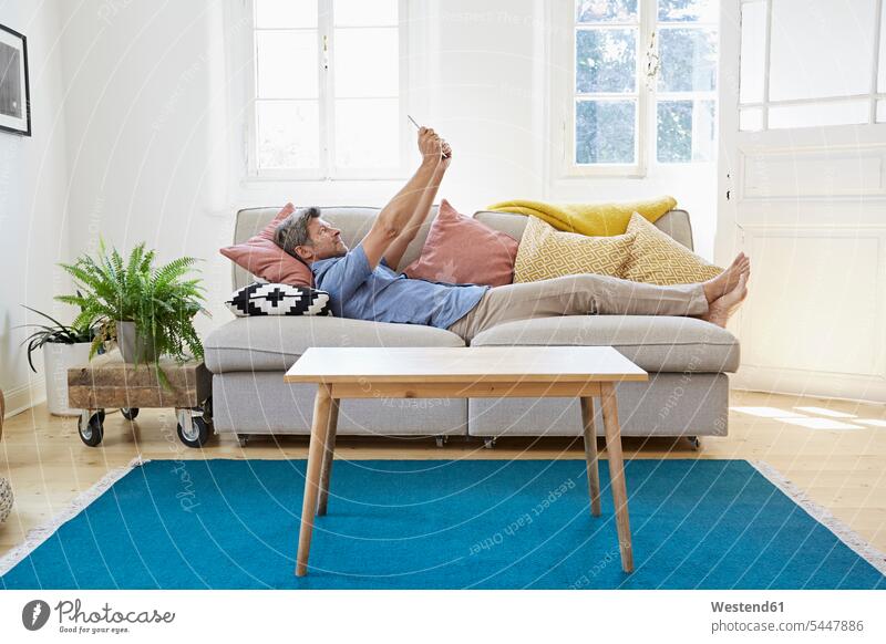 Man lying on couch at home, using digital tablet online Surfing the Net comfortable man men males relaxation relaxed relaxing Internet The Internet technology