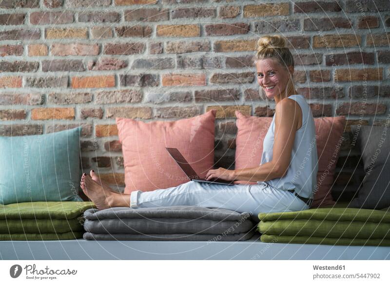Mature woman sitting on couch, usine laptop Laptop Computers laptops notebook females women working At Work settee sofa sofas couches settees Seated home