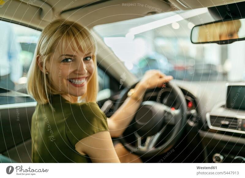 Blond woman choosing new car in car dealership female customer automobile Auto cars motorcars Automobiles select choose selecting car dealerships buying blond