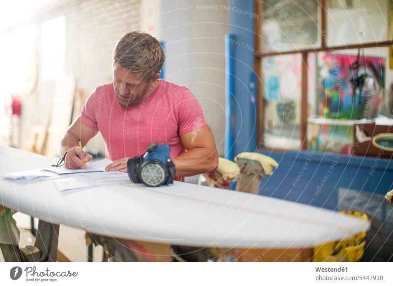 Surfboard shaper workshop, surfshop employee filling out paper work man men males surfboard surfboards working At Work writing write Adults grown-ups grownups