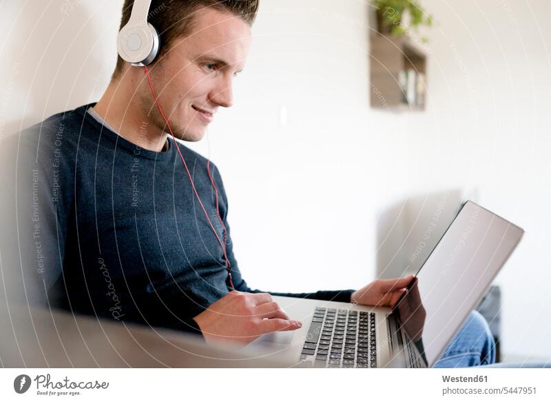 Man using laptop and headphones at home man men males living room living rooms livingroom headset Laptop Computers laptops notebook Adults grown-ups grownups
