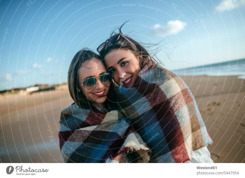 Portrait of two women covered with blanket on the beach female friends portrait portraits beaches mate friendship Sea ocean best friend bff best friends wrapped