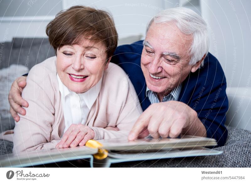 Senior couple lying on couch, looking at photo album senior adults seniors old photograph photographs photos photograph album photo albums watching laying down