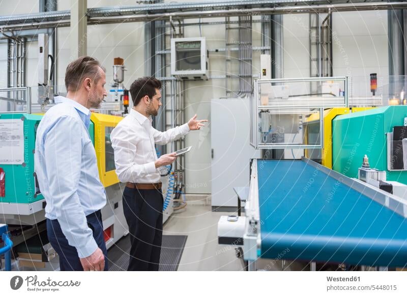 Two men in factory talking at machine Businessman Business man Businessmen Business men colleagues factories business people businesspeople business world