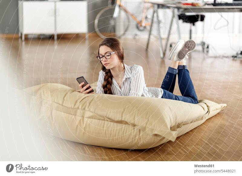 Young woman with cell phone lying in bean bag in office laying down lie lying down offices office room office rooms mobile phone mobiles mobile phones Cellphone