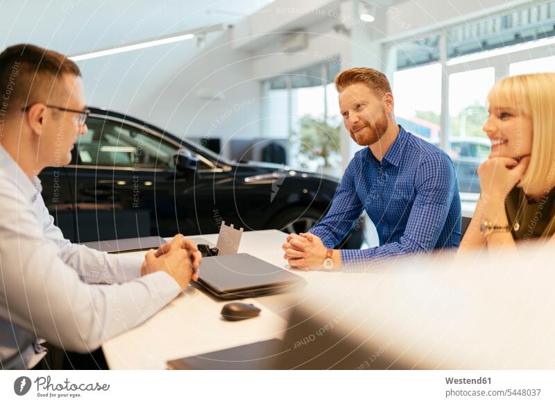 Salesperson advising couple in car dealership automobile Auto cars motorcars Automobiles selling seller sellers car dealerships buying discussing discussion