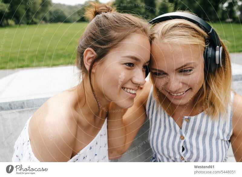 Two smiling young women sharing headphones outdoors female friends headset smile woman females happiness happy share mate friendship Adults grown-ups grownups