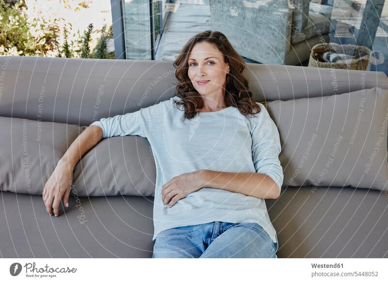 Woman sitting relaxed on couch at terrace woman females women relaxation Seated happiness happy terraces content pleased settee sofa sofas couches settees home