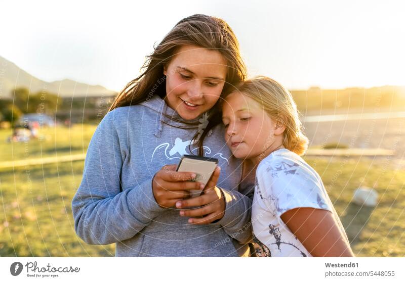 Two girls looking at cell phone outdoors females female friends Smartphone iPhone Smartphones child children kid kids people persons human being humans