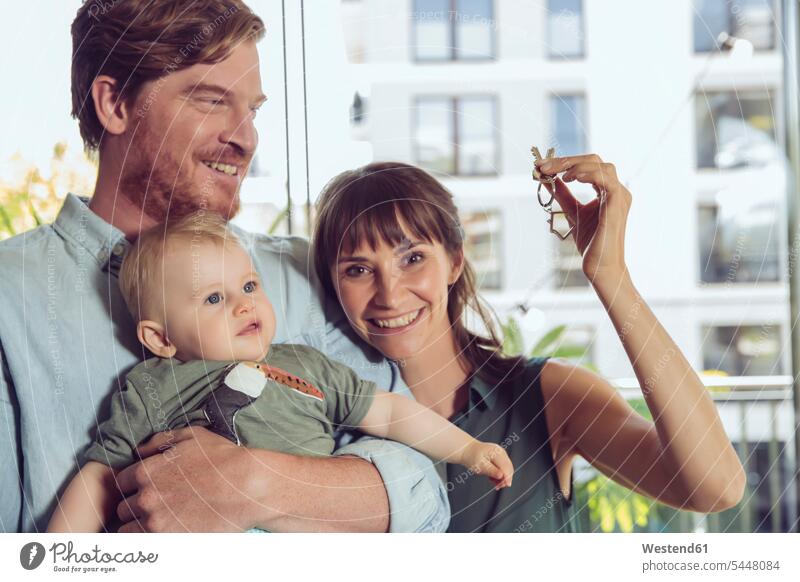 Happy couple with baby holding house key apartment flats apartments keys smiling smile twosomes partnership couples infants nurselings babies happiness happy