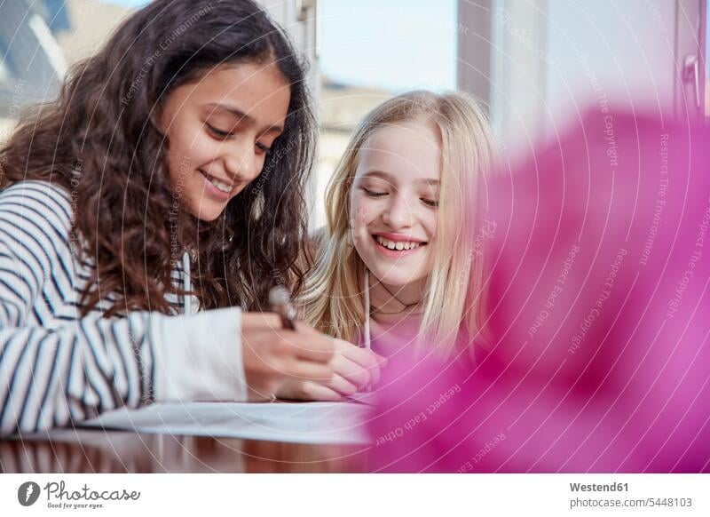 Two girls doing homework together smiling smile females Home work writing write female friends child children kid kids people persons human being humans
