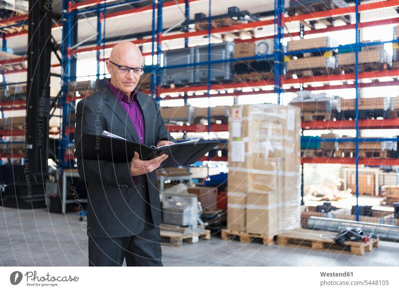 Businessman with documents on factory shop floor factories males folder file folders portfolio portfolios files Adults grown-ups grownups adult people persons