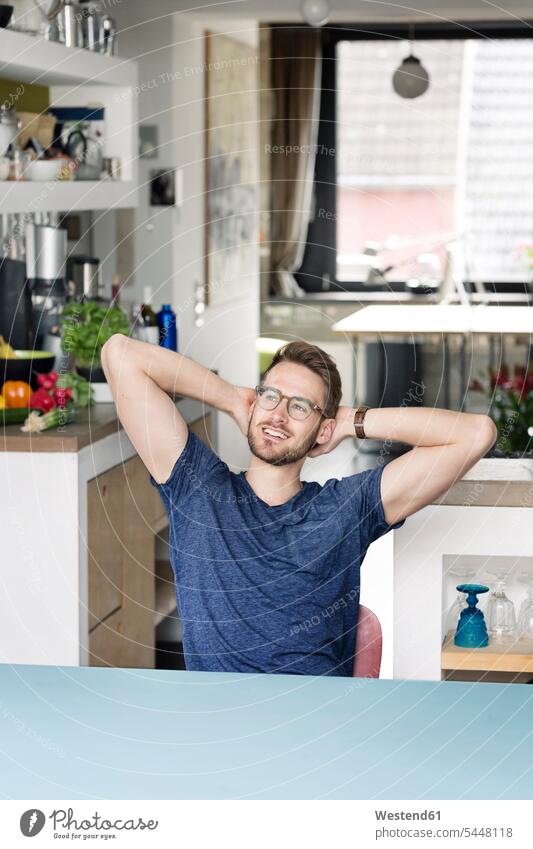 Portrait of smiling young man sitting at kitchen table at home Table Tables men males Seated smile portrait portraits domestic kitchen kitchens Adults grown-ups