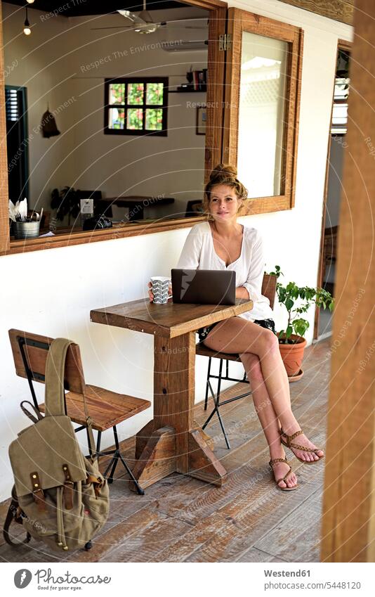 Portrait of young woman with laptop and mug of coffee sitting on veranda of a coffee shop Laptop Computers laptops notebook computer computers cafe Seated
