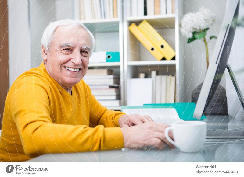 Senior man working at computer with a cup of coffee sitting Seated At Work drinking Coffee men males computers senior men senior man elder man elder men