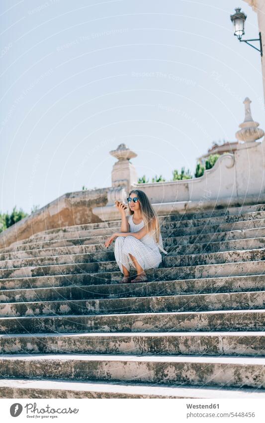 Spain, Valencia, woman sitting on stairs using smartphone Seated stairway use females women Smartphone iPhone Smartphones mobile phone mobiles mobile phones
