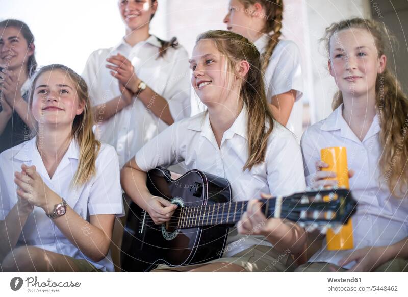 Female high school student playing guitar with group of school friends outside schoolgirl female pupils School Girl schoolgirls School Girls guitars education