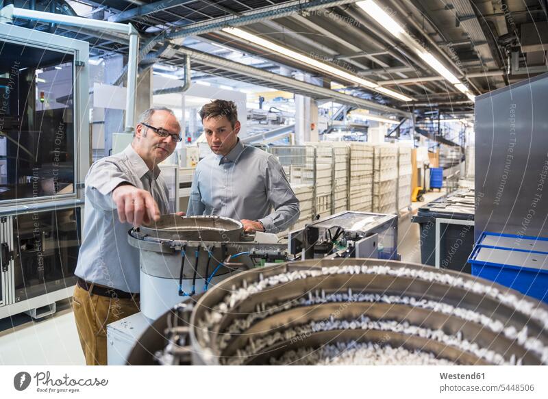 Two men in factory shop floor examining outcome of a machine talking speaking factories colleagues man males Adults grown-ups grownups adult people persons