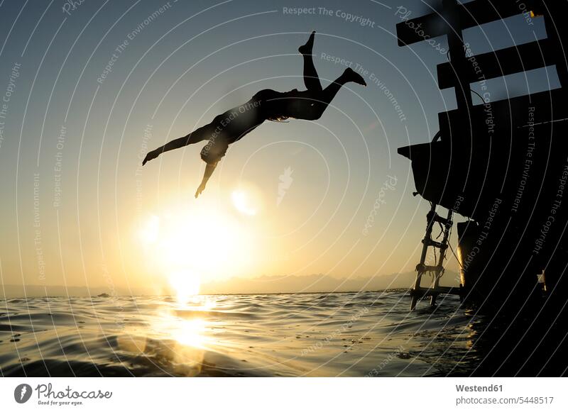 Man jumping fom jetty into the sea at sunset ocean man men males Leaping vacation Holidays water waters body of water Adults grown-ups grownups adult people