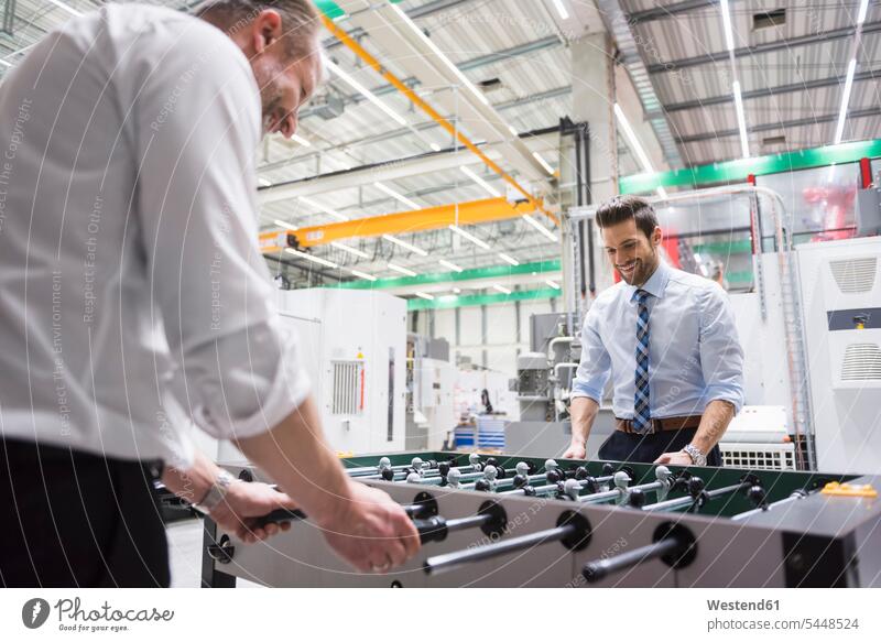 Two colleagues playing foosball in factory smiling smile factories Businessman Business man Businessmen Business men business people businesspeople