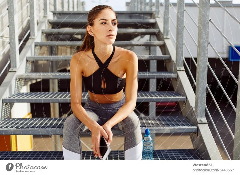 Woman taking break from workout and holding cell phone on stairs sitting Seated exercising exercise training practising stairway woman females women Adults
