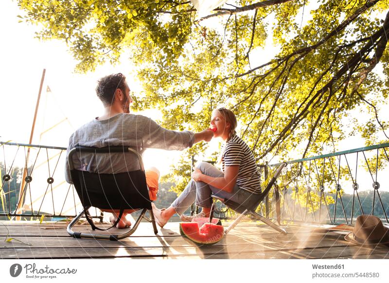 Young couple sitting on a jetty at a lake eating watermelon jetties Seated Watermelon Watermelons Water Melon Water Melons twosomes partnership couples Fruit