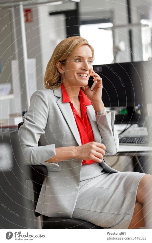 Businesswoman at desk in office on cell phone smiling smile offices office room office rooms on the phone call telephoning On The Telephone calling mobile phone