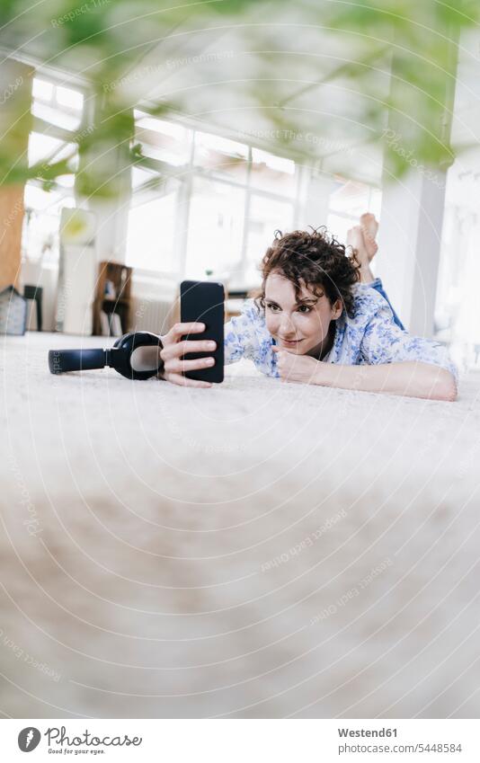 Woman lying on floor in her apartment, using smartphone flat flats apartments Selfie Selfies laying down lie lying down woman females women headphones headset