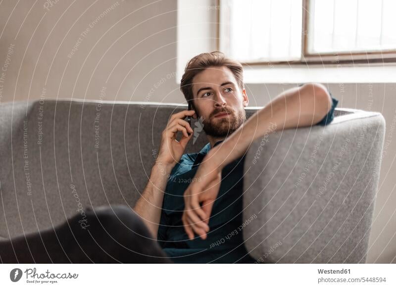 Portrait of young man on the phone sitting on couch men males call telephoning On The Telephone calling Adults grown-ups grownups adult people persons