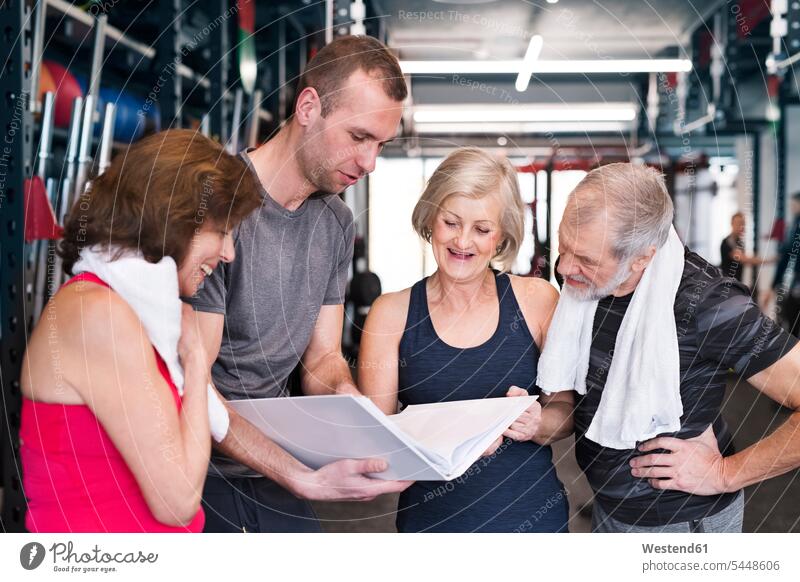 Group of fit seniors and personal trainer in gym looking in folder senior adults eyeing gyms Health Club Adults grown-ups grownups people persons human being