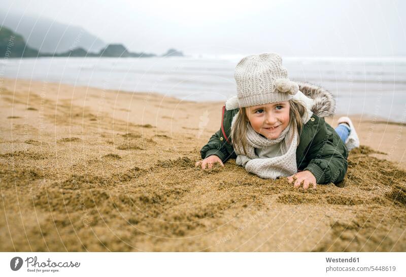 Happy girl lying in sand on the beach in winter sandy females girls beaches happiness happy laying down lie lying down child children kid kids people persons